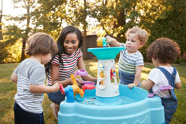 Child care provider and children outside at a water table