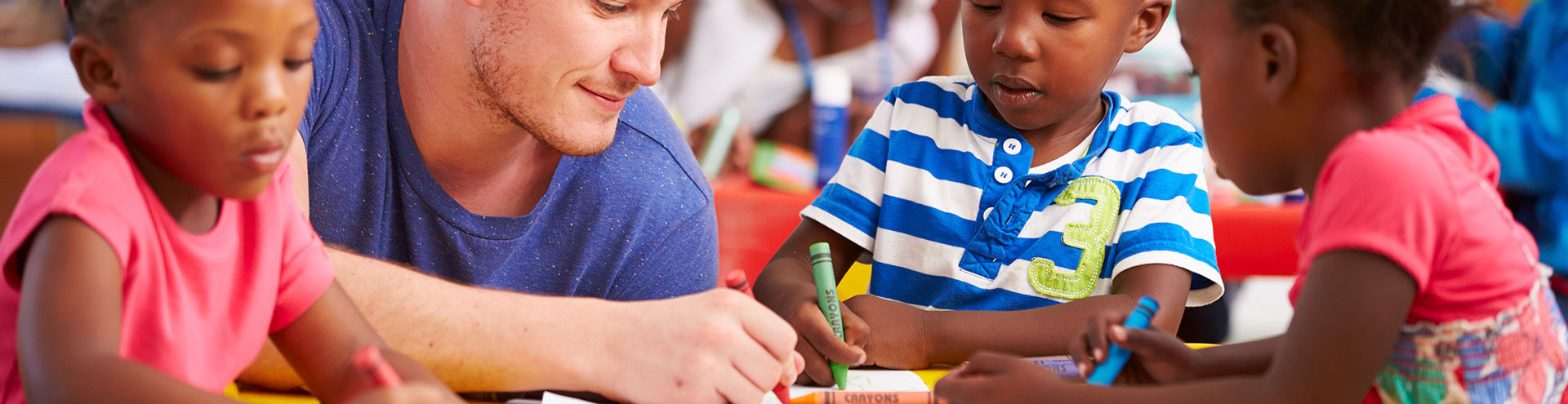 male teacher colors with crayons alongside toddlers
