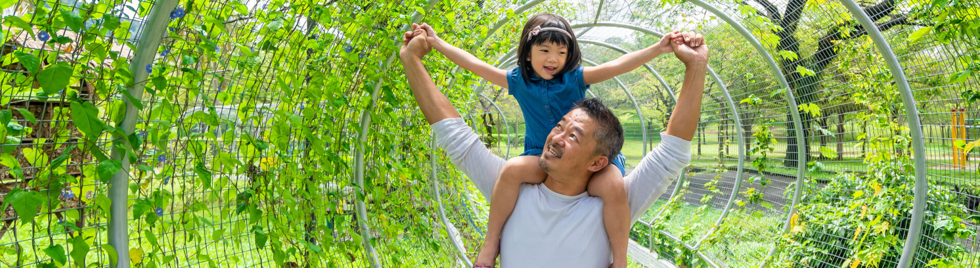 Father holding his daughter hand on his shoulder and having fun with his daughter in the park.