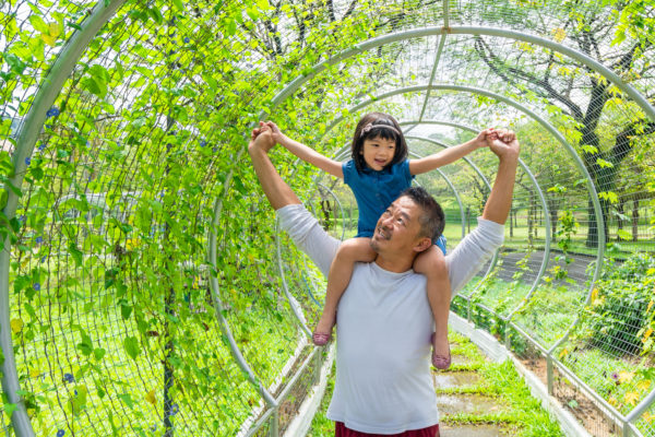 Father holding his daughter hand on his shoulder and having fun with his daughter in the park.