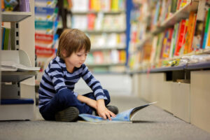 Adorable little child, boy, sitting in a book store, reading books